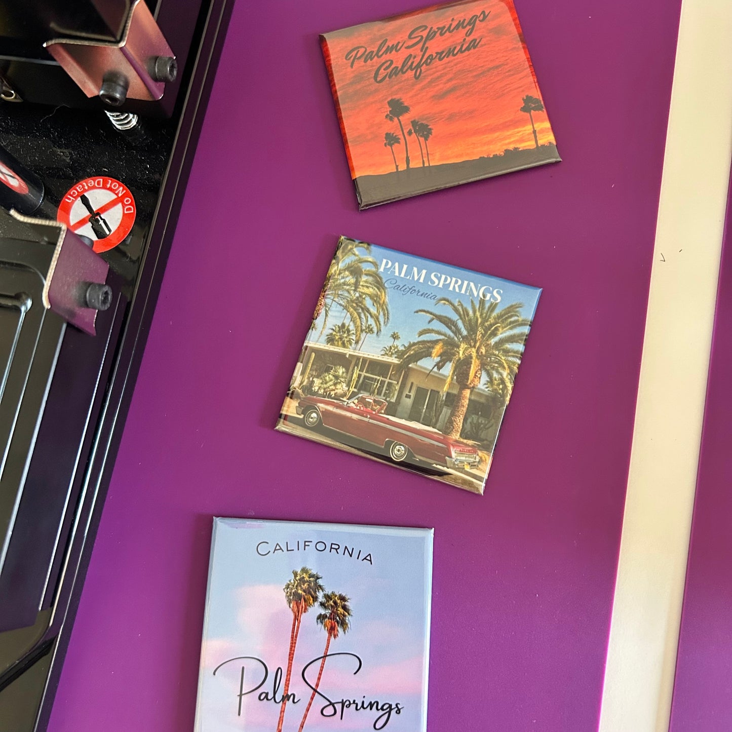 Three 'Palm Springs, California' themed magnets on a purple surface.
