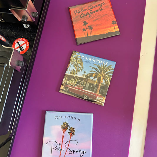 Three 'Palm Springs, California' themed magnets on a purple surface.