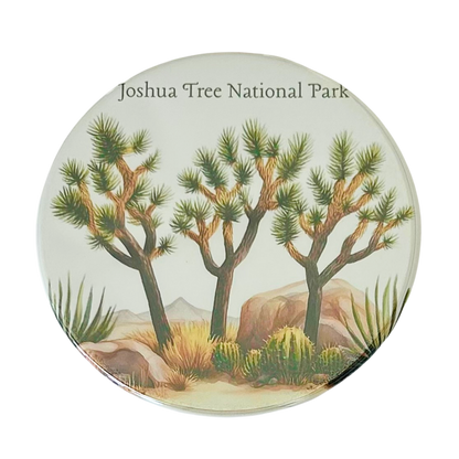Square coaster featuring a watercolor illustration of three Joshua trees with agave plants, desert scrub, and boulders under the text "Joshua Tree National Park."

