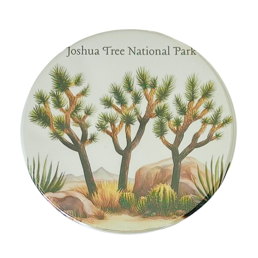Square coaster featuring a watercolor illustration of three Joshua trees with agave plants, desert scrub, and boulders under the text "Joshua Tree National Park."


