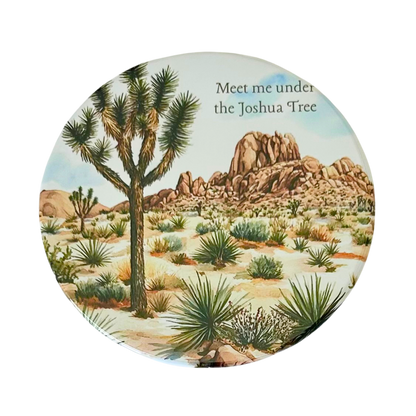 Square coaster featuring a watercolor desert landscape with a Joshua tree, yucca plants, boulder formations, and the text "Meet me under the Joshua Tree."
