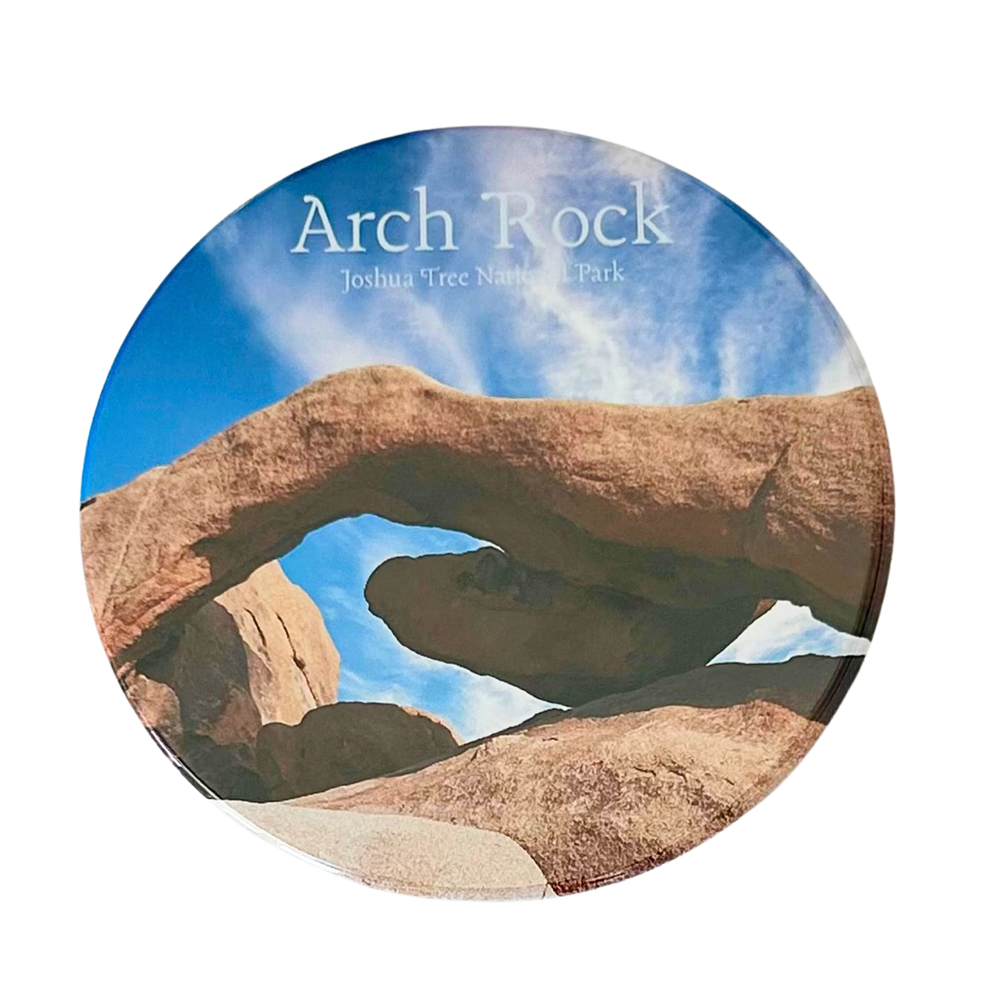 Square coaster featuring a close-up photo of Arch Rock at Joshua Tree National Park — a sweeping granite arch framing a bright blue sky with wispy clouds.