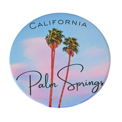 Round 3.5" Palm Springs California coaster featuring two tall palm trees against a soft blue and pink pastel sky, with "California" in block letters and "Palm Springs" in elegant script.