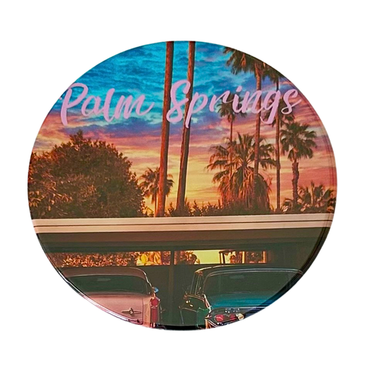 Round 3.5" Palm Springs coaster featuring two classic vintage cars, one pink and one teal, parked at sunset with silhouetted palms and a dreamy pink and orange sky.