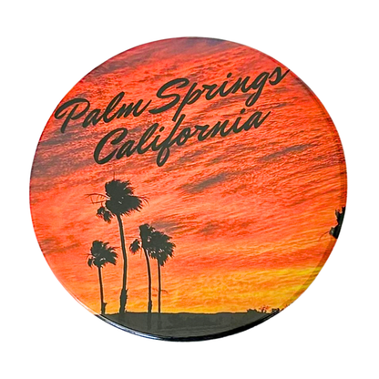 Round 3.5" Palm Springs California coaster featuring silhouetted palm trees against a dramatic orange and red sunset sky with bold script lettering.