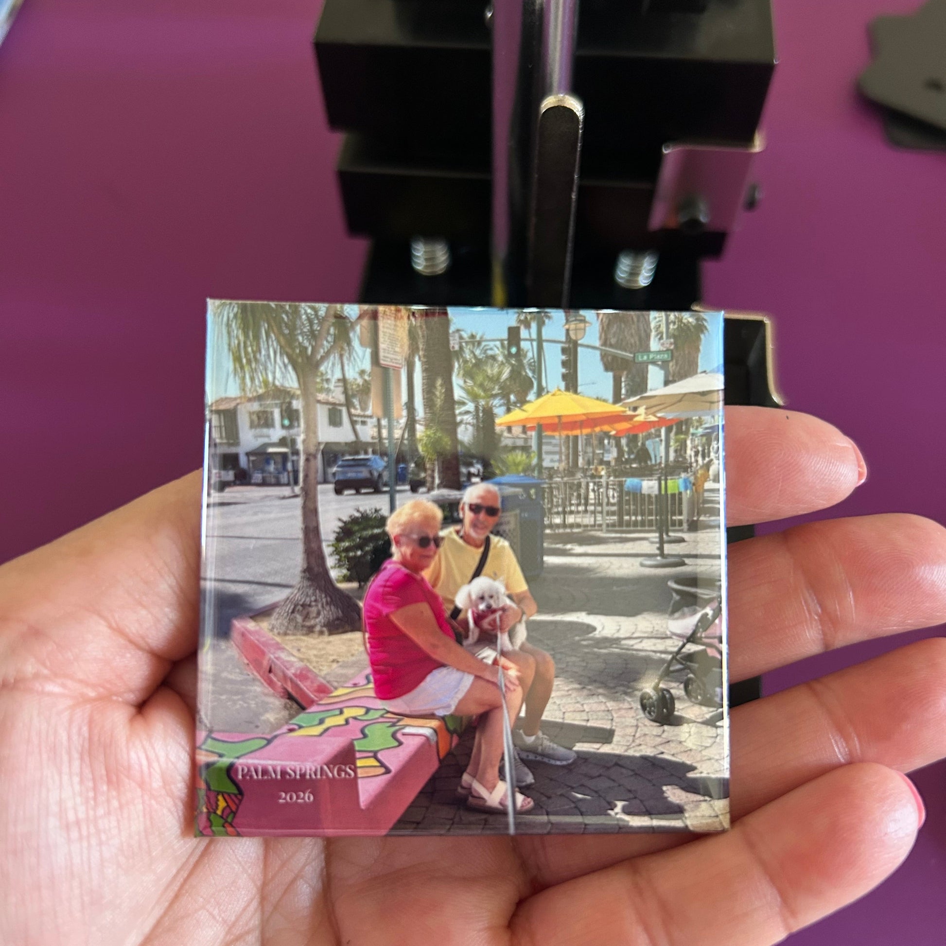 Hand holding a small square magnet  with a colorful design against a purple background