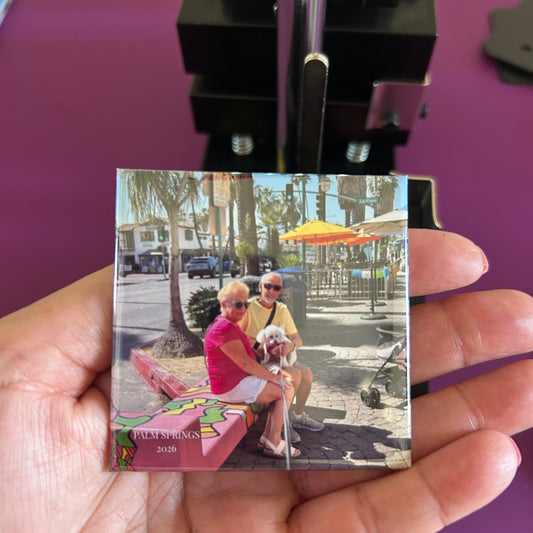 Hand holding a small square magnet  with a colorful design against a purple background